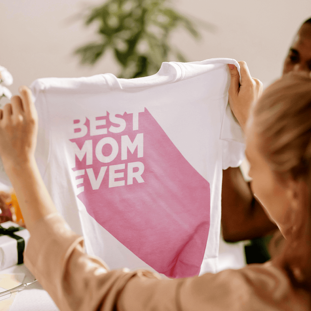 Excited mother holding shirt that says best Mom Ever